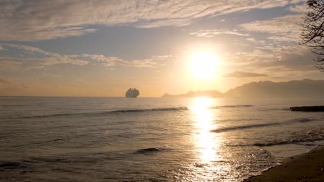 Un-Gran-Crucero-Con-Turistas-Que-Visitan-La-Ciudad-Amarrado-En-La-Costa-De-La-Capital-Dili,-Timor-Leste-En-El-Sudeste-Asiático-Al-Amanecer-Dorado-Sobre-El-Paisaje-Oceánico