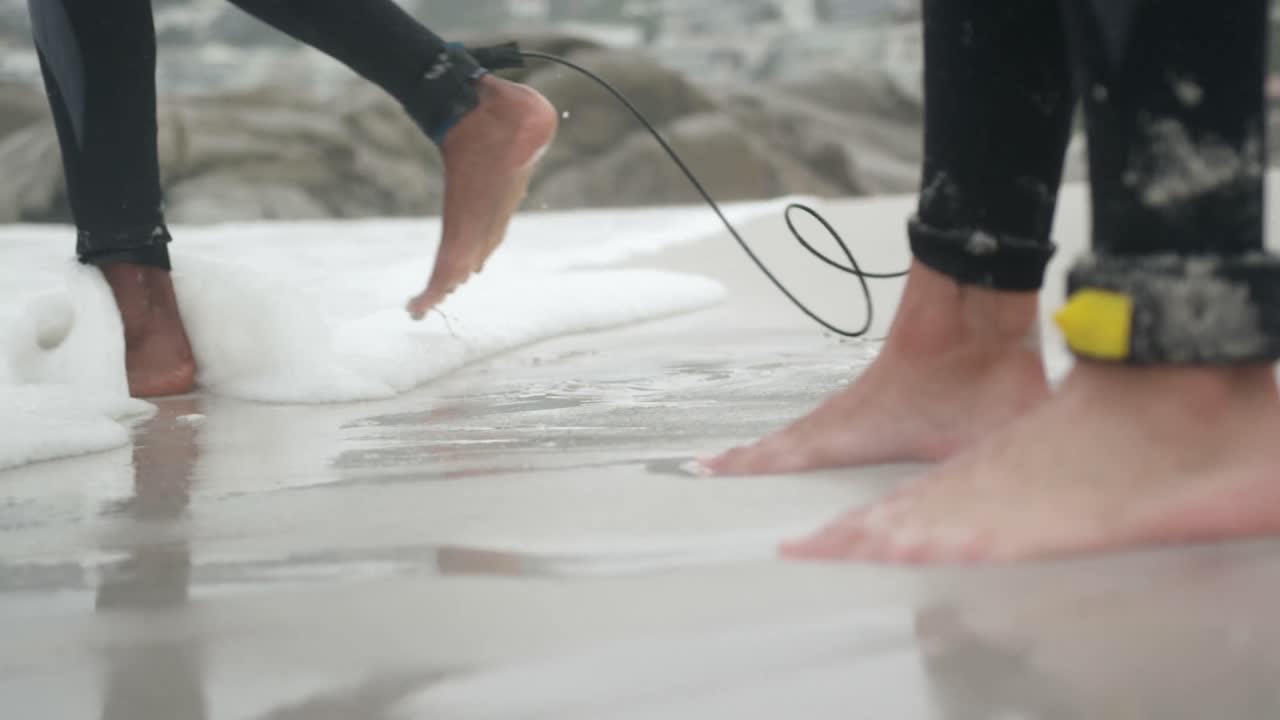Low section of two male surfers standing barefoot on the beach 4k