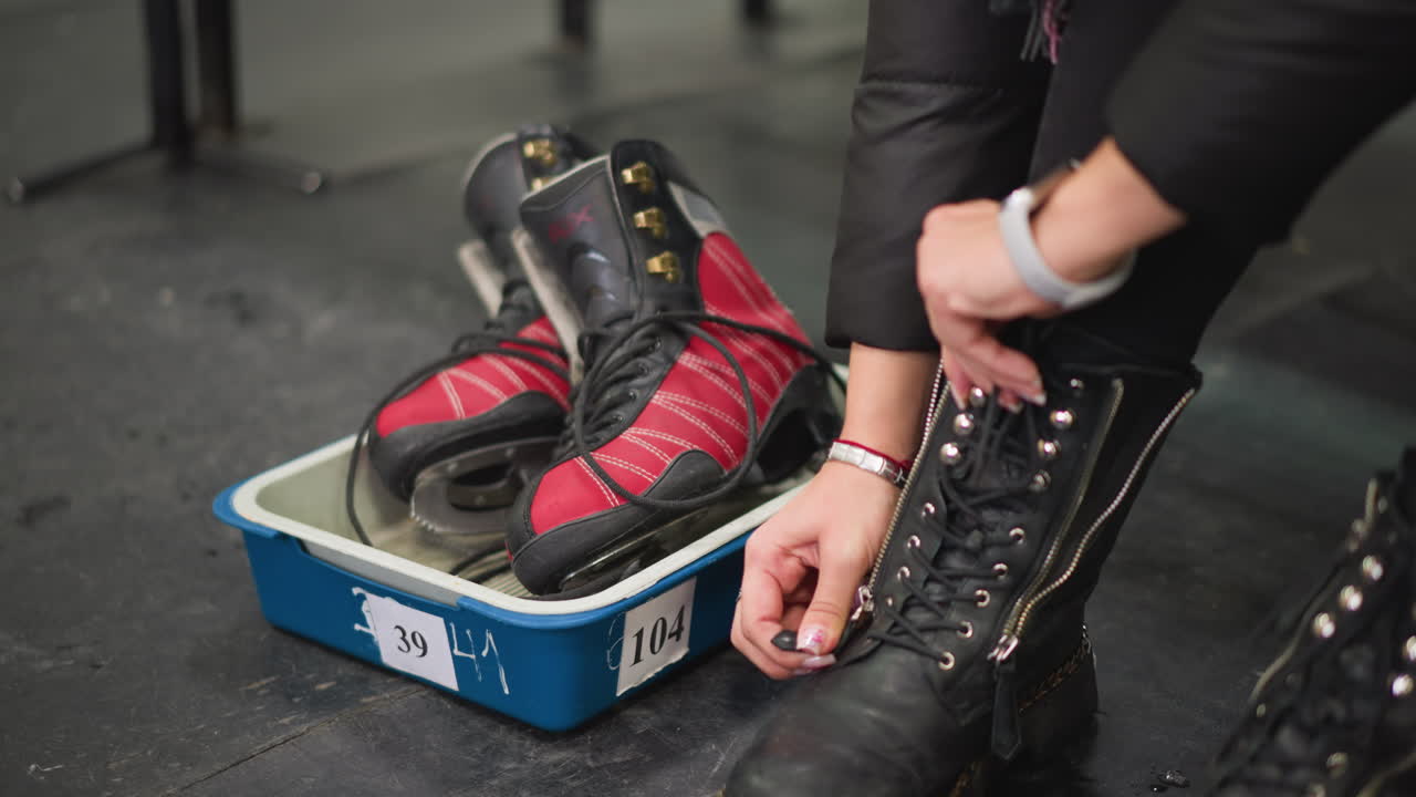 Hand changing shoe with black leather boot featuring zipper and chain detail on wet scratched floor indoor environment visible marks water stains preparation moment for winter activity footwear transition scene