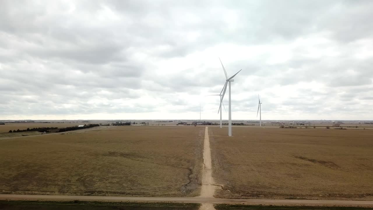 Slow aerial approach along a gravel road to a small grouping of wind turbines in a winter field in rural Nebraska