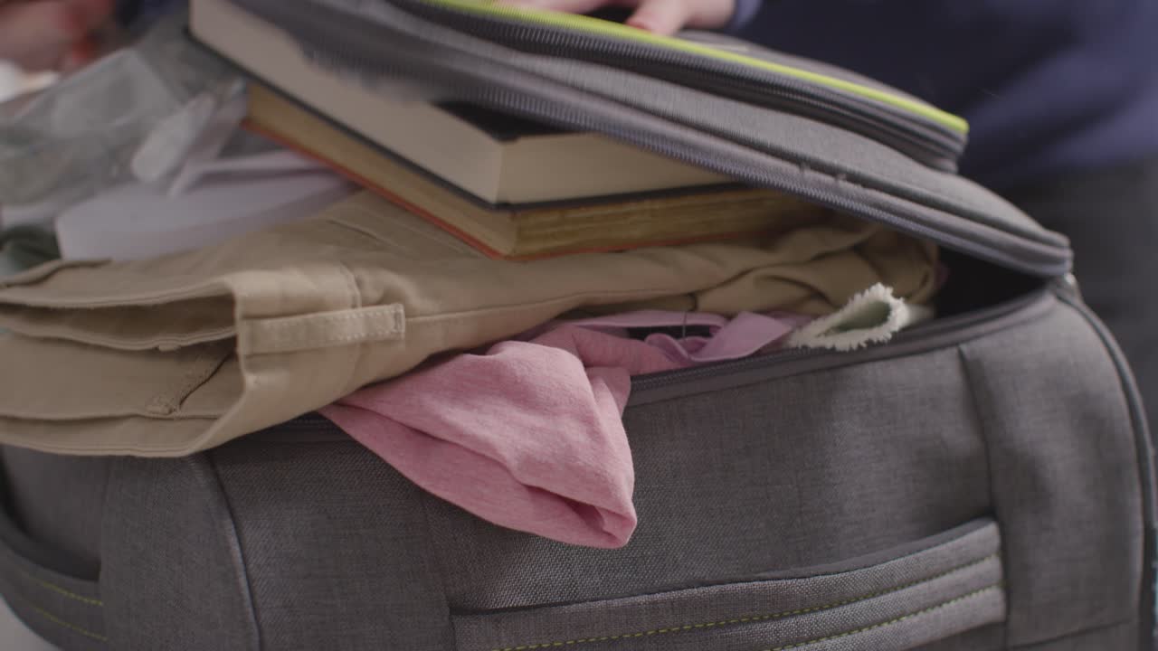 primer plano de una persona empacando libros de ropa y chanclas en una maleta lista para las vacaciones de verano