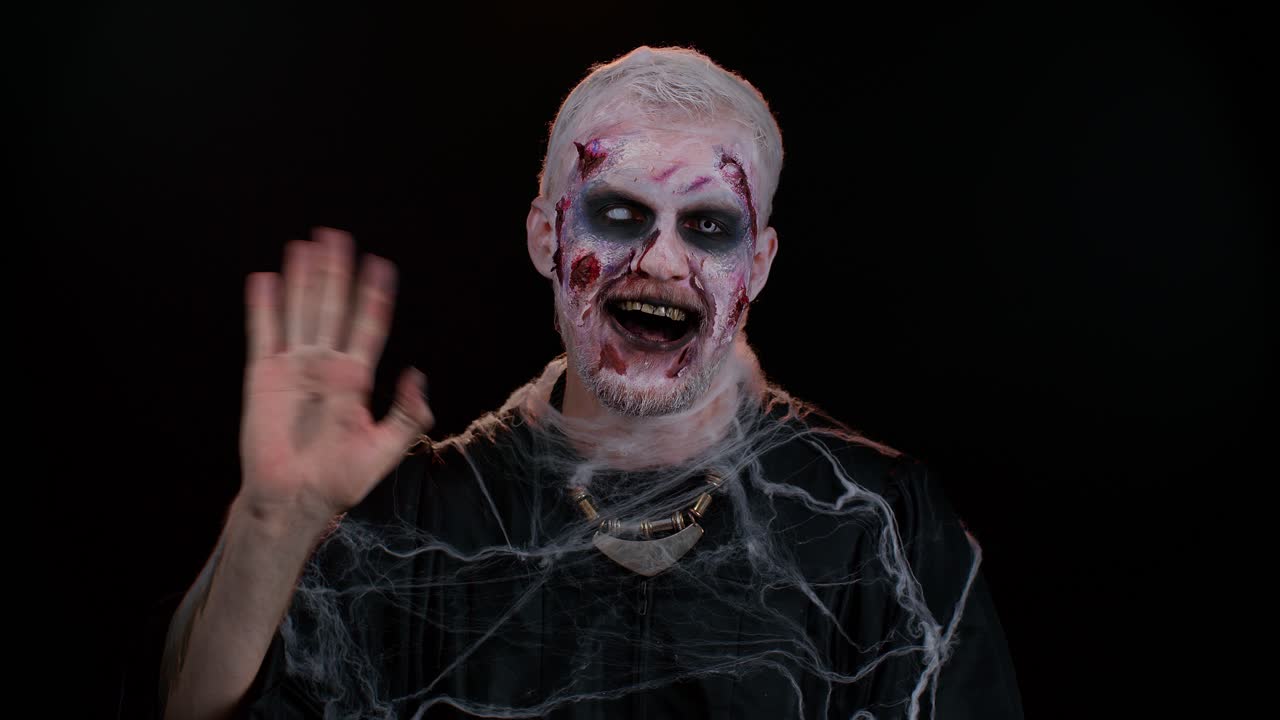 espeluznante halloween hombre zombi sonriendo amistosamente agitando las manos gestando hola o adiós, bienvenida