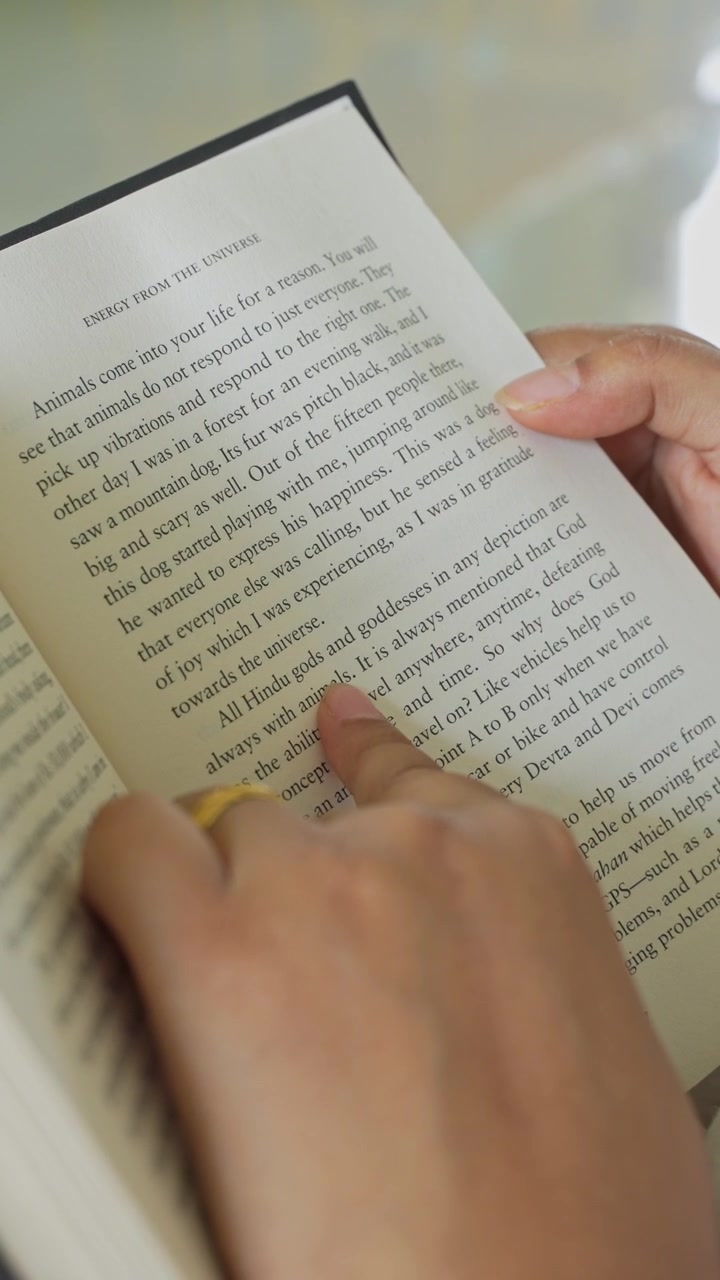 Close-up of a woman's hand gently pressing and smoothing an open book page while reading, with clearly visible printed text and soft natural window light illuminating.