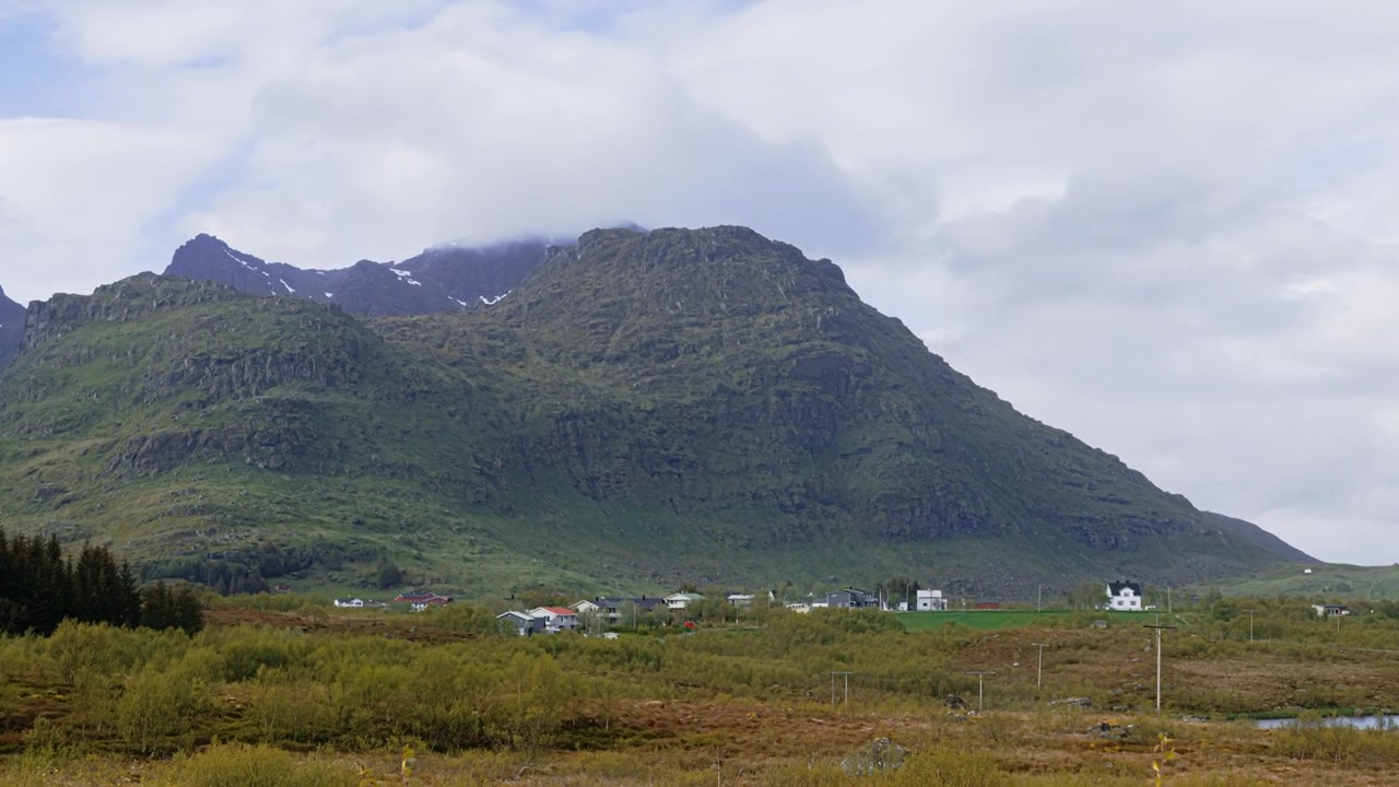 En panorerende time-lapse-optagelse af en lille landsby omkring en sø omgivet af bjerge på en overskyet dag nær Leknes, en by midt på Lofoten-øerne, Norge