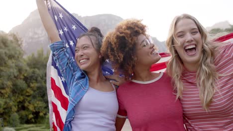 porträt von glücklichen, vielfältigen freundinnen, die die flagge der usa halten und im garten feiern, slow motion