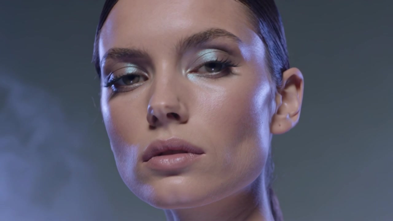 Blinking female model tilting head and adjusting gaze in studio with blue shadow, fog and sparkle
