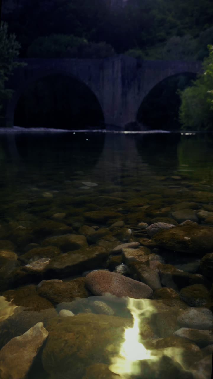 An old stone bridge casts a perfect reflection on a calm twilight river.