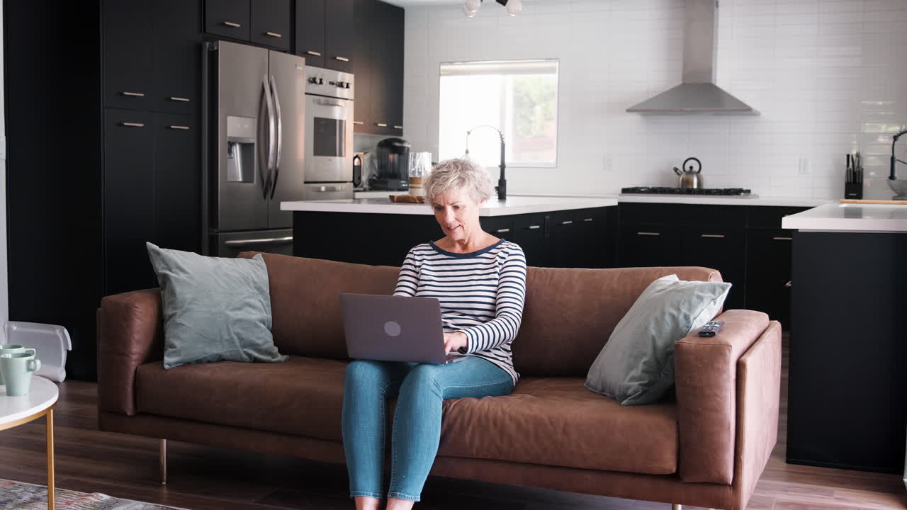 Senior white woman sitting on couch using laptop computer