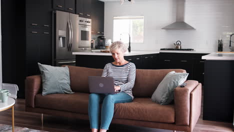 Senior-white-woman-sitting-on-couch-using-laptop-computer