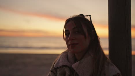 Cinematic-close-up-shot-of-woman-looking-at-camera-with-golden-sky-sunset-background-on-the-beach