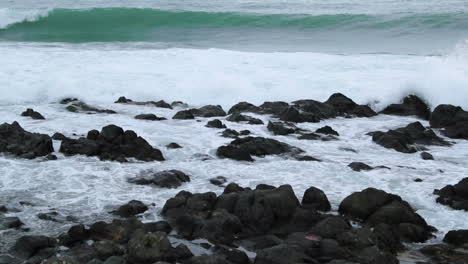vista de primer plano de rocas en alta mar estrelladas por fuertes olas marinas y reflexionando sobre y a través de piedras durante el día en captura de cámara lenta a 120 fps
