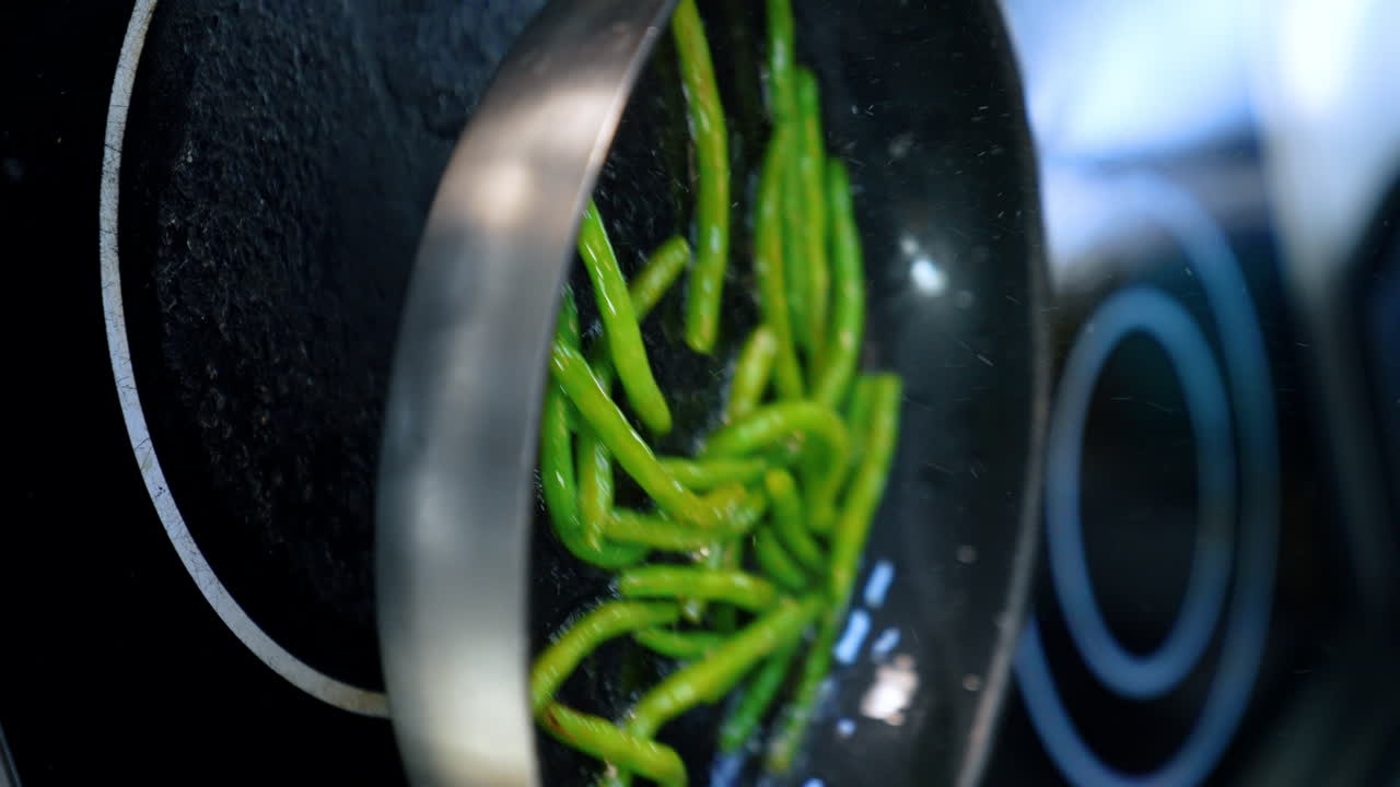 Mixing green beans during the frying on the pan. Preparation of vegetables close up. Vertical screen.