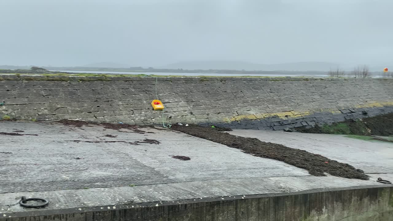 Pan across old Tarrea Pier with seaweed and over turned small boat on cloudy grey day