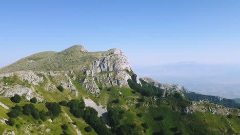 vuelo del avión no tripulado alrededor del pico de la montaña rocosa y un pequeño bosque a gran altitud