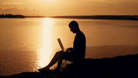 man sit and work on the laptop by sunset (sunrise) background on the top of the hill