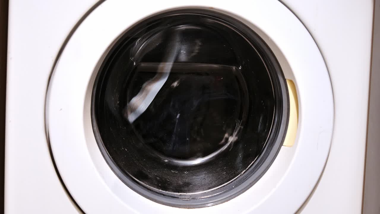 Washing machine drum spins laundry at high speed through round glass window