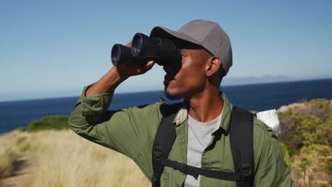 hombre afroamericano caminando por la costa usando binoculares