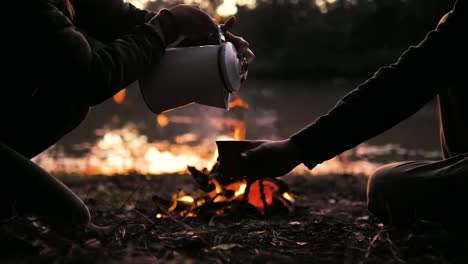 camping in the forest pouring hot water in the cup in front of the fireplace in the evening