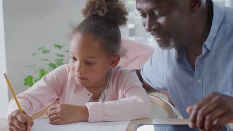 grandfather helping granddaughter with home schooling sitting at table with digital tablet