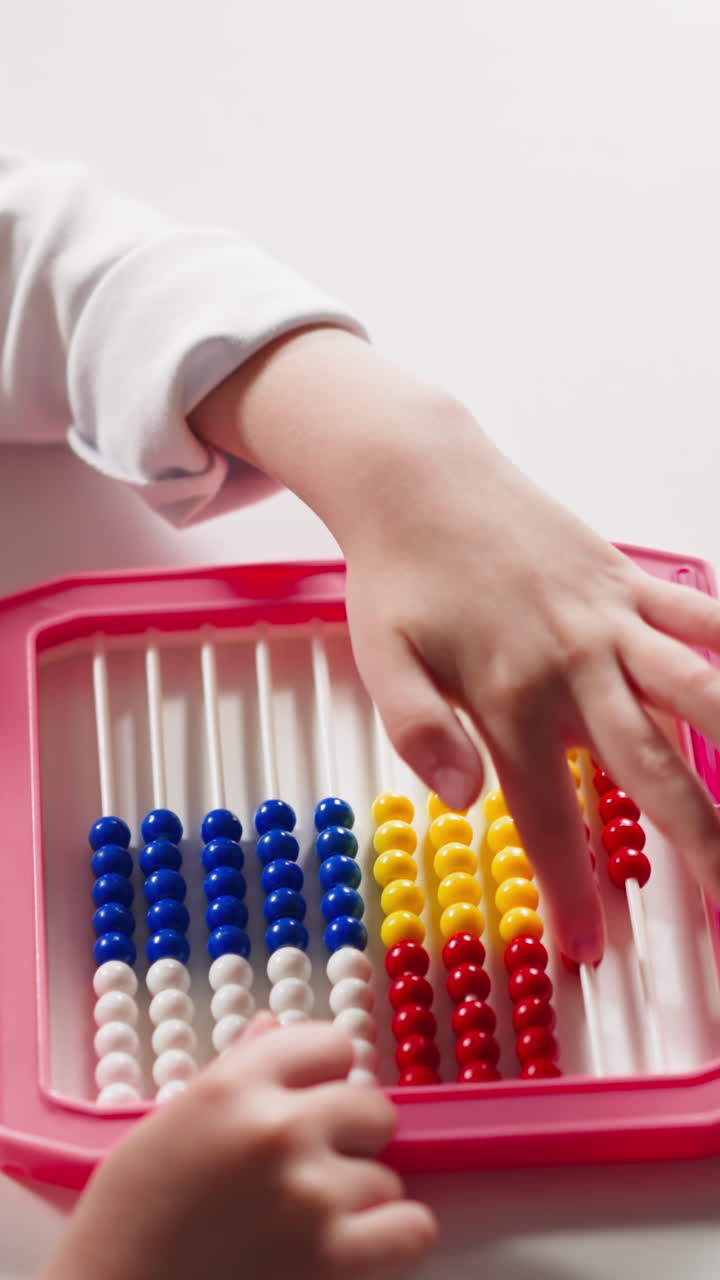 Cute little schoolgirl does sums moving plastic beads by left hand finger on colorful abacus at arithmetic lesson at home upper closeup slow motion