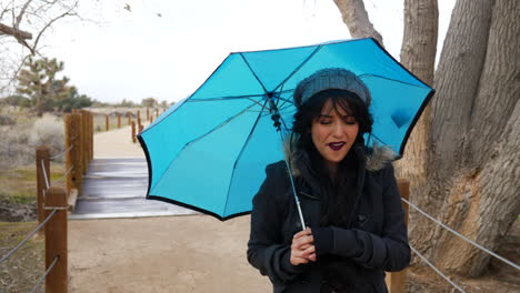 una linda mujer sonriendo y caminando en una tormenta con un paraguas azul para protegerla de los fuertes vientos y el mal tiempo a cámara lenta