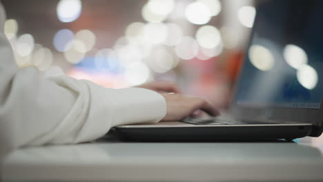 close-up of hand typing on laptop keyboard in modern indoor setting, with blurred figure walking in colorful bokeh-filled background