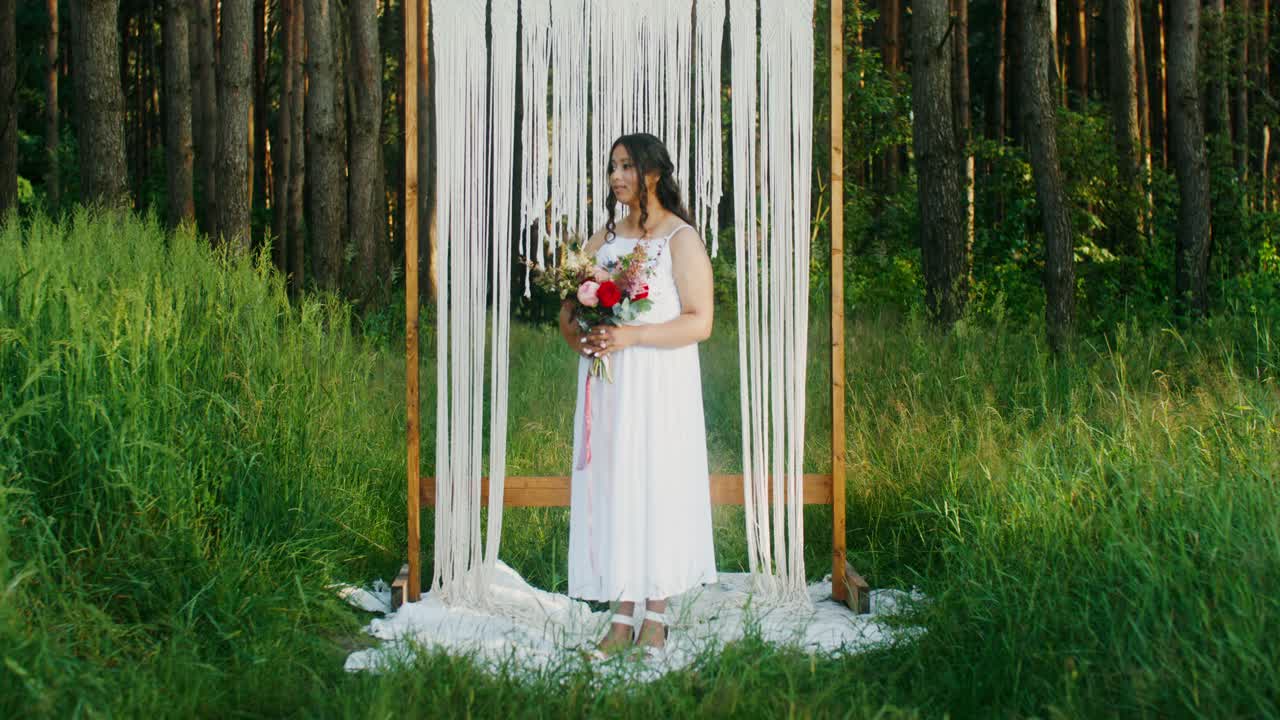 Donna in abito bianco con un bouquet di fiori in una foresta
