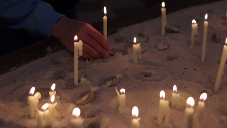 worshiper place prayer candle on sand inside a church - close up