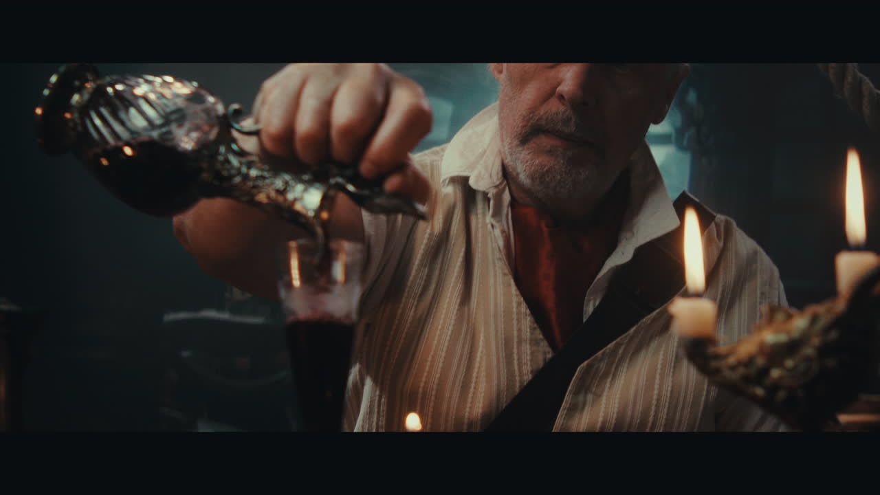 An old pirate eats and drinks inside the sailing ship cabin