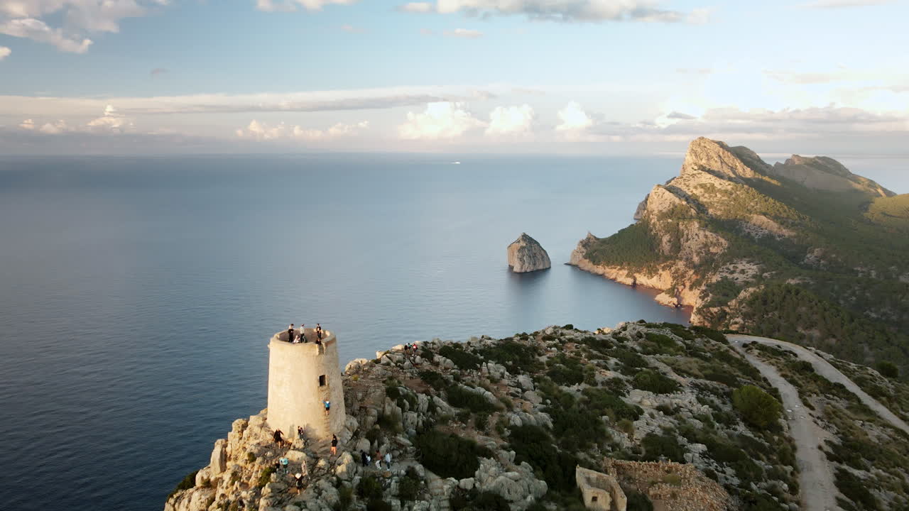 Un drone si muove in avanti oltre la Torre di Albercutx su una scogliera rocciosa verso la penisola di Cap Formentor e il faraglione sul mare aperto sopra il Mar Mediterraneo calmo durante l'ora d'oro