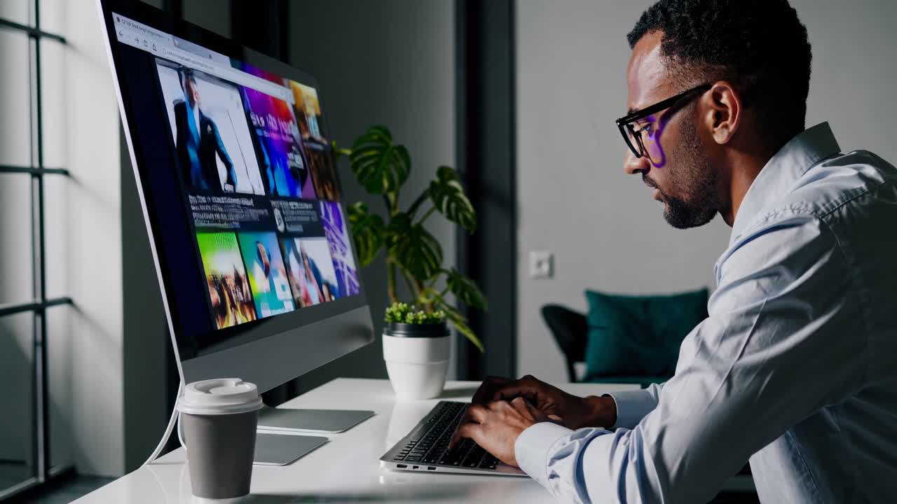 Side angle of a man working on a computer, browsing video content