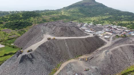 un dron aéreo disparó lejos de una montaña de escombros sueltos con camiones volquete descargando más desechos rocosos de un proyecto de túnel en una región montañosa que afecta la ecología y el terreno locales