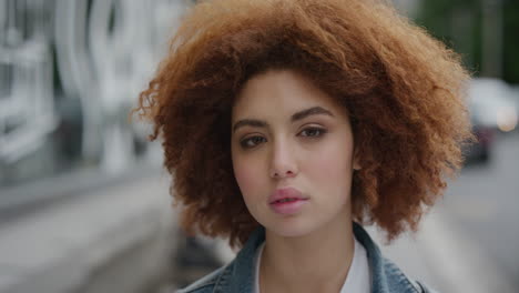 portrait of beautiful young mixed race woman looking at camera pensive calm cute female student red afro frizzy hairstyle in urban city street