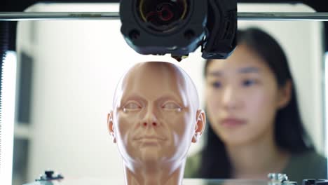 a close-up view of a 3d printer fabricating a realistic synthetic head with a focused operator in the background observing the process