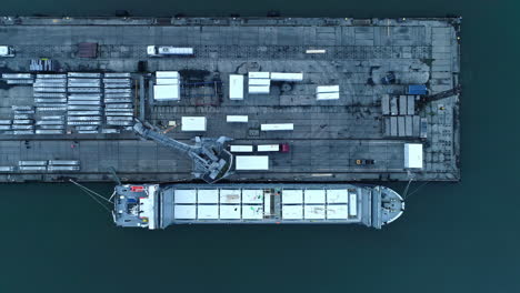 Aerial-top-down-shot-of-crane-transporting-goods-on-container-ship-at-port