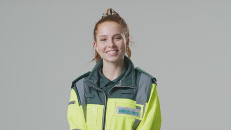 studio portrait of smiling young female paramedic against plain background