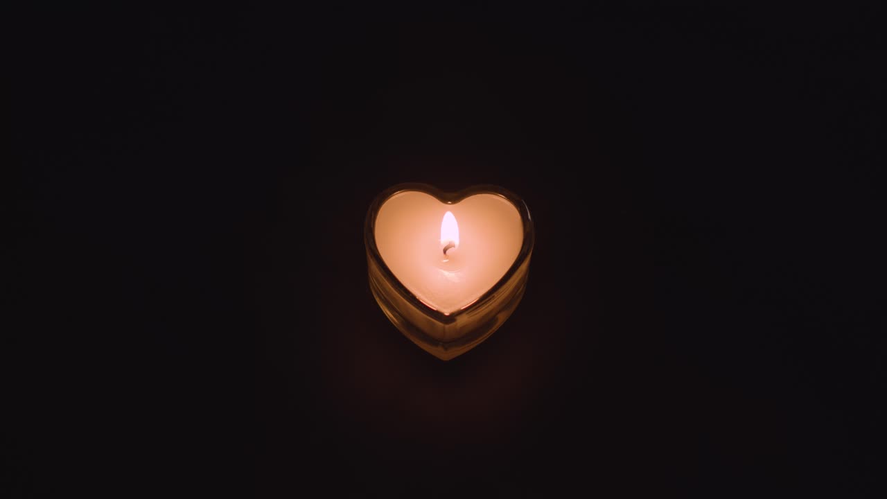 una vela blanca en forma de corazón romántica encendida sobre un fondo negro que se apaga
