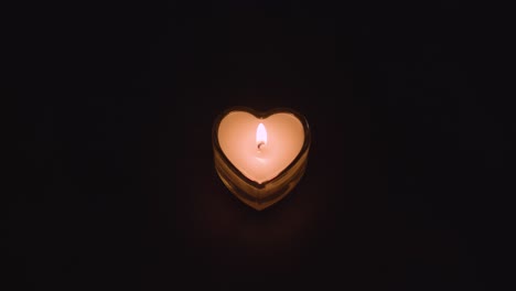 Romantic-Lit-Heart-Shaped-White-Candle-On-Black-Background-Being-Blown-Out