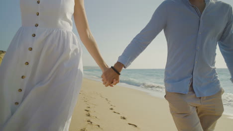 sección media de una pareja cogida de las manos en una playa de arena