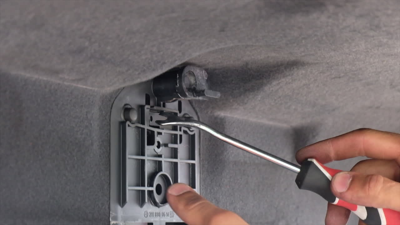 Close up of a man using a screwdriver to word on a part of the trunk of a car