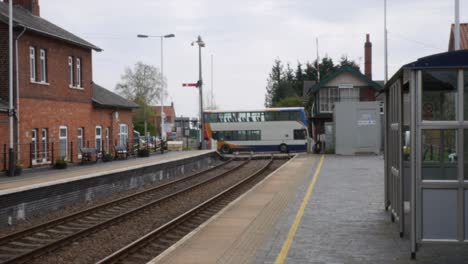 un autobús de dos pisos cruzando las vías del tren en una antigua estación de tren de pueblo en inglaterra