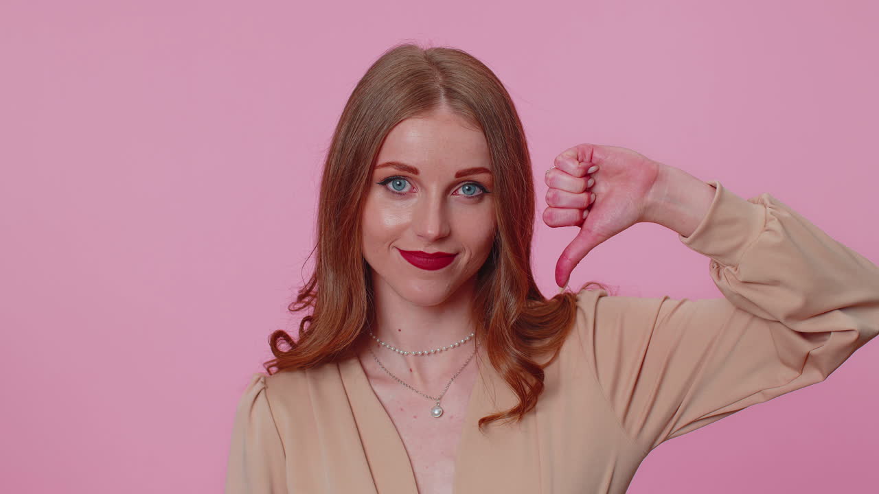 베이지 블라우스를 입은 화가 난 소녀가 엄지손가락을 아래로 보이고 신호 제스처, 불쾌감, 불만족, 혐오감을 나타니다.