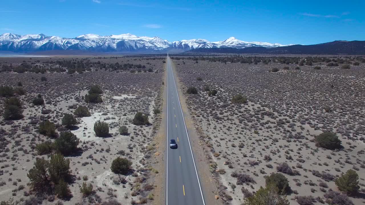 Luftfoto af en 4WD, der kører på en asfalteret vej i Mojave-ørkenen med Sierra Nevada-bjergene i det fjerne 1.