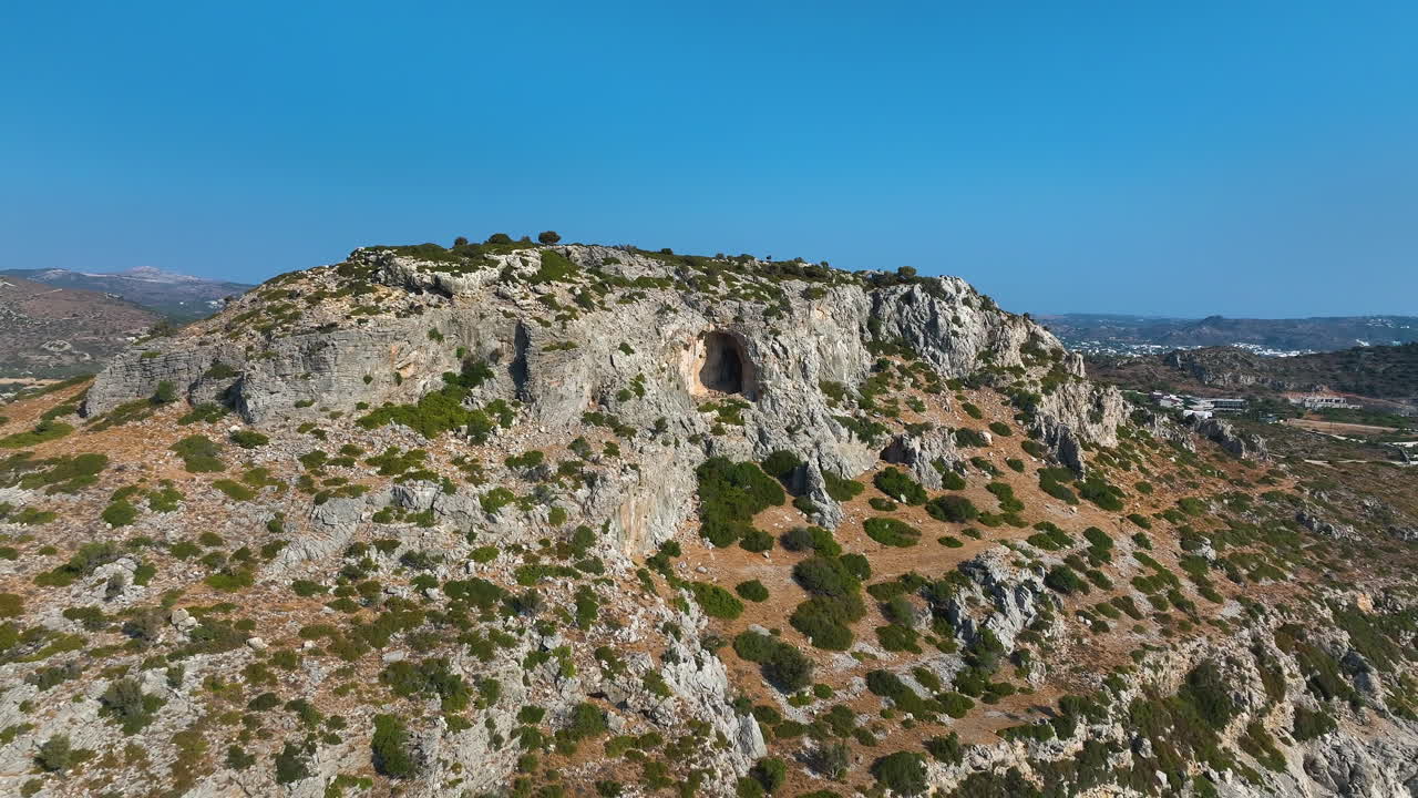 Aerial pull back away from a mountain cave, sunny morning in Rhodes, Greece