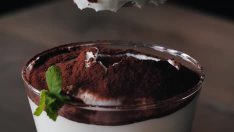 close-up, taking a spoon of a white cream dessert covered with cacao powder and a mint garnish