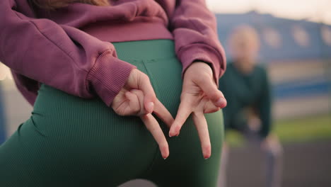 close up buttocks view of lady slightly bent with hand pointing out with slight view of other ladies in background engaged in fitness or stretching exercises outdoors