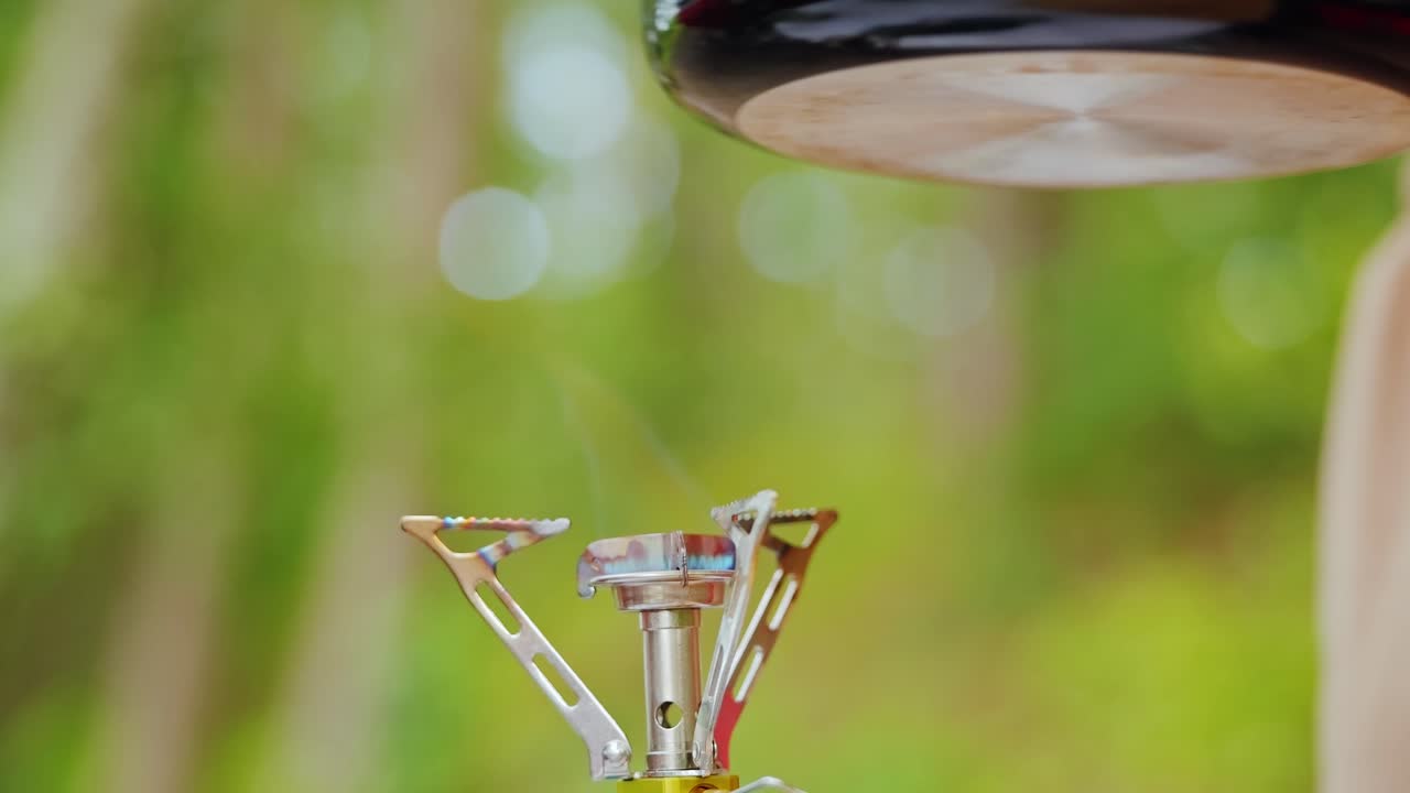 Close up on female hands removing frying pan from gas stove in forest campsite