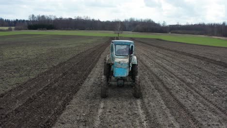 Front-view-of-old-soviet-tractor-with-farmer-inside,-plow-garlic-furrows