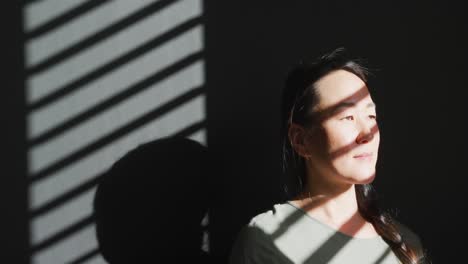 thoughtful asian woman sitting on sofa close to window at home