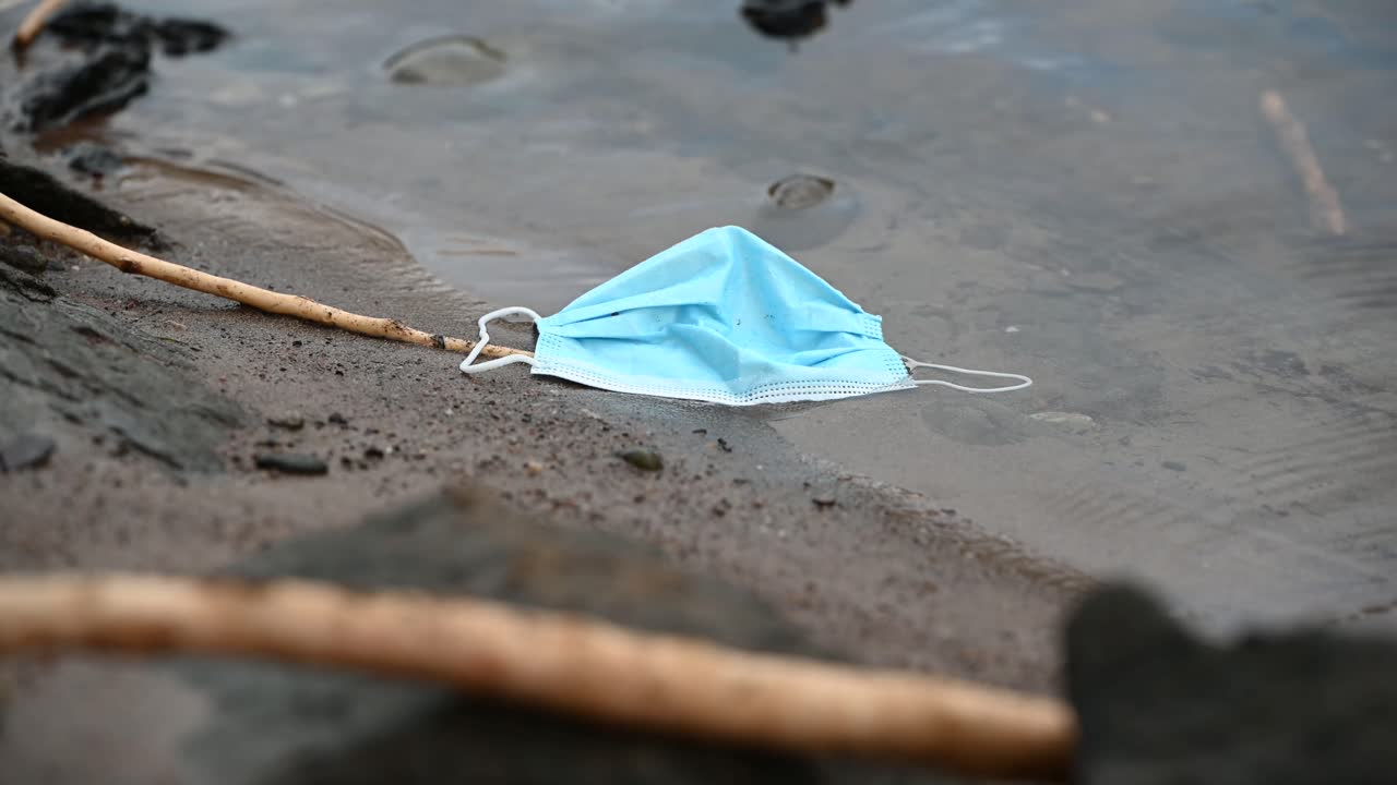 Wet and dirty medical face mask lying on the river bank on an overcast day